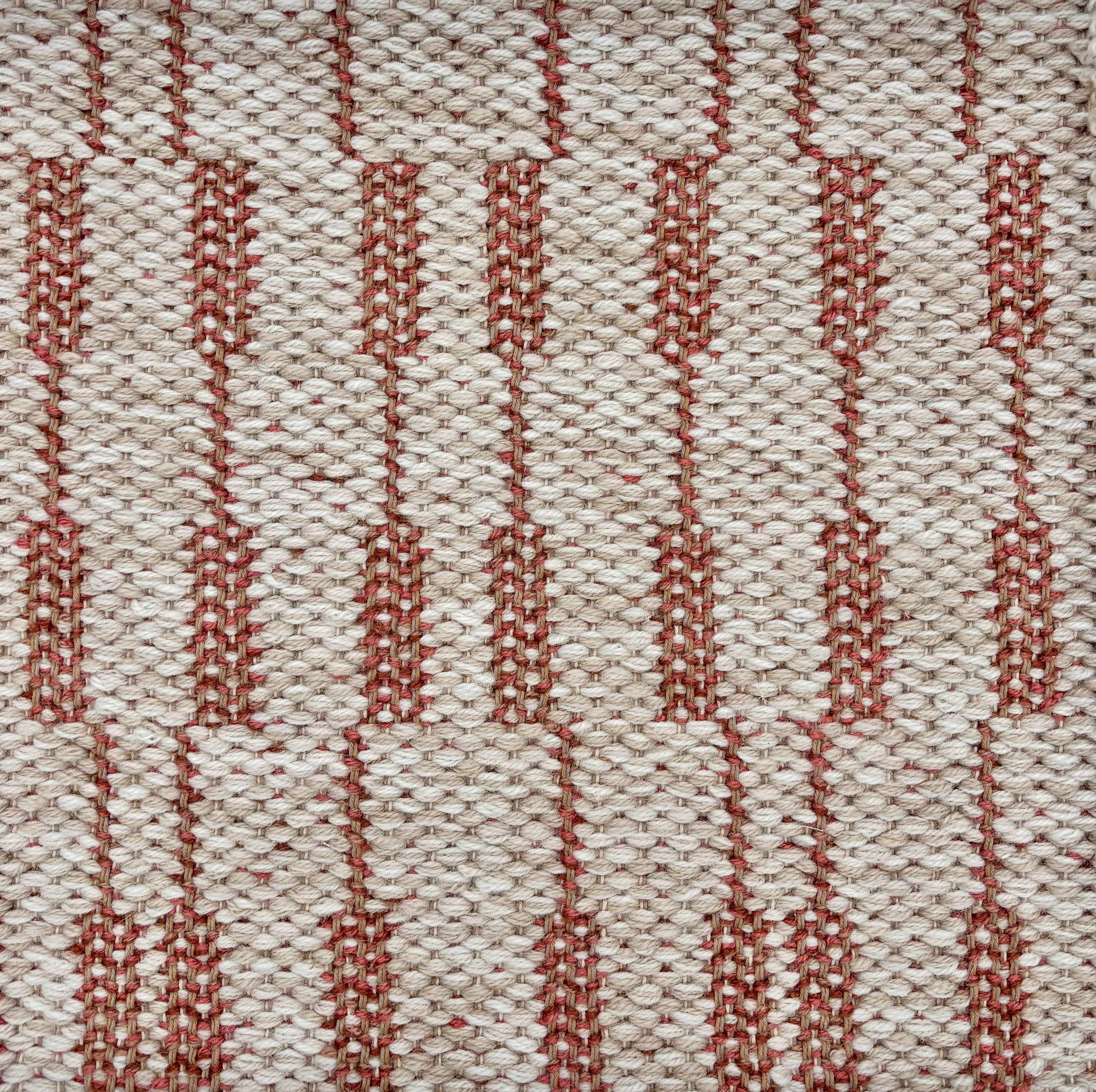 Handwoven rug sample in an oatmeal field with a stacked rust red and brown stripe. 