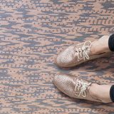 Detail of handwoven leather rug in a graphic geometric pattern in tan and grey with seated woman's legs and oxford shoes. 