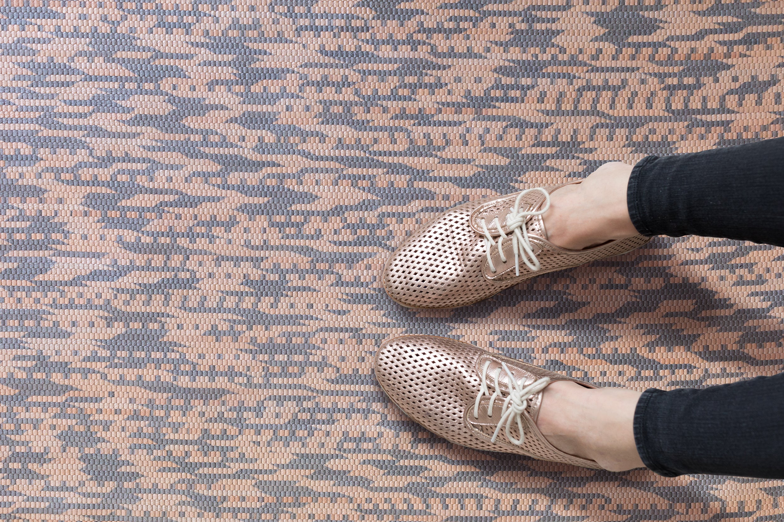 Detail of handwoven leather rug in a graphic geometric pattern in tan and grey with seated woman's legs and oxford shoes. 
