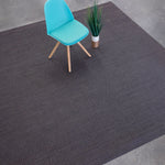Overhead shot of a chair sitting on a woven leather rug in a herringbone pattern in mottled gray with pink accents.