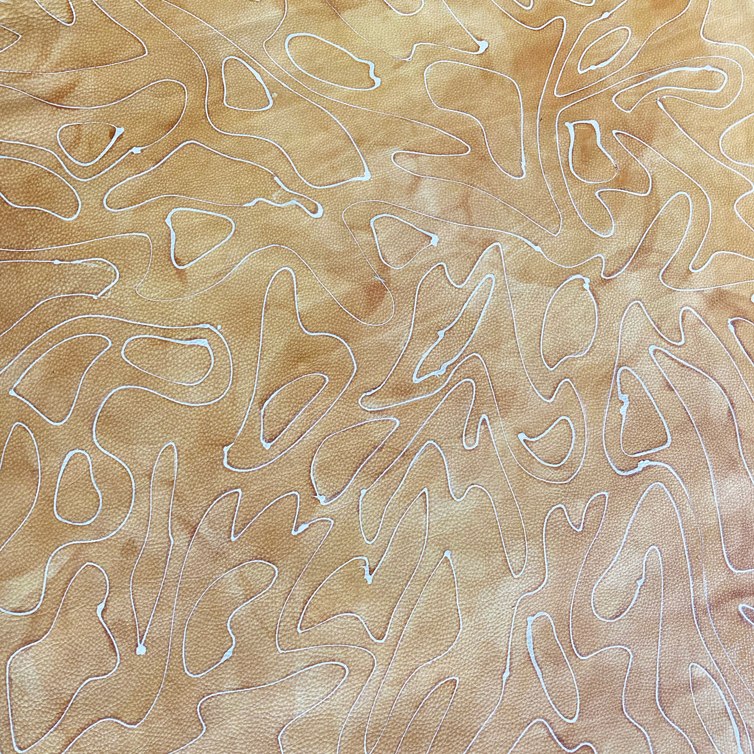 Close-up of cowhide upholstery leather in mottled tan with a white curvilinear overlay.