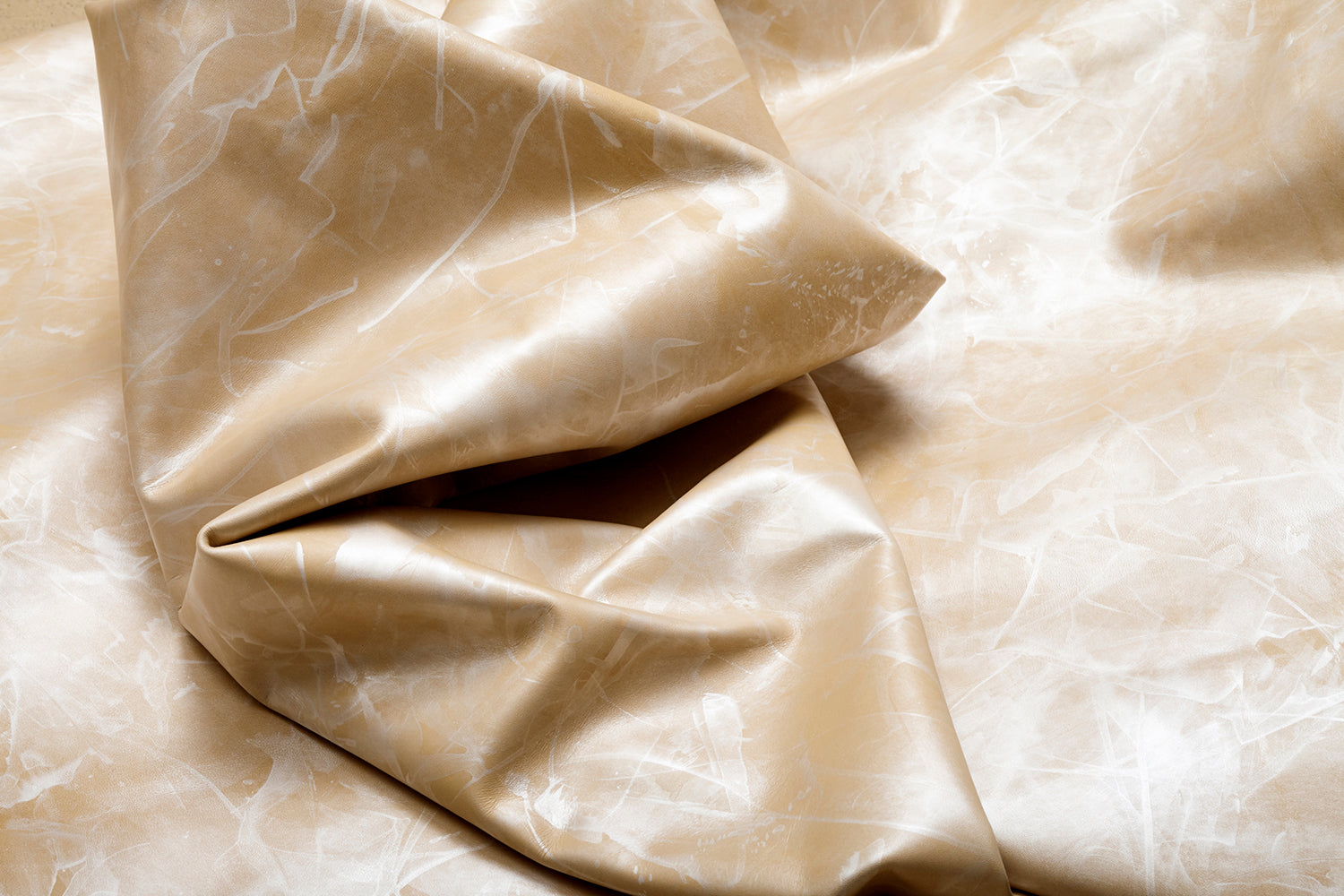 Draped upholstery leather in a mottled textural pattern in tan and white.