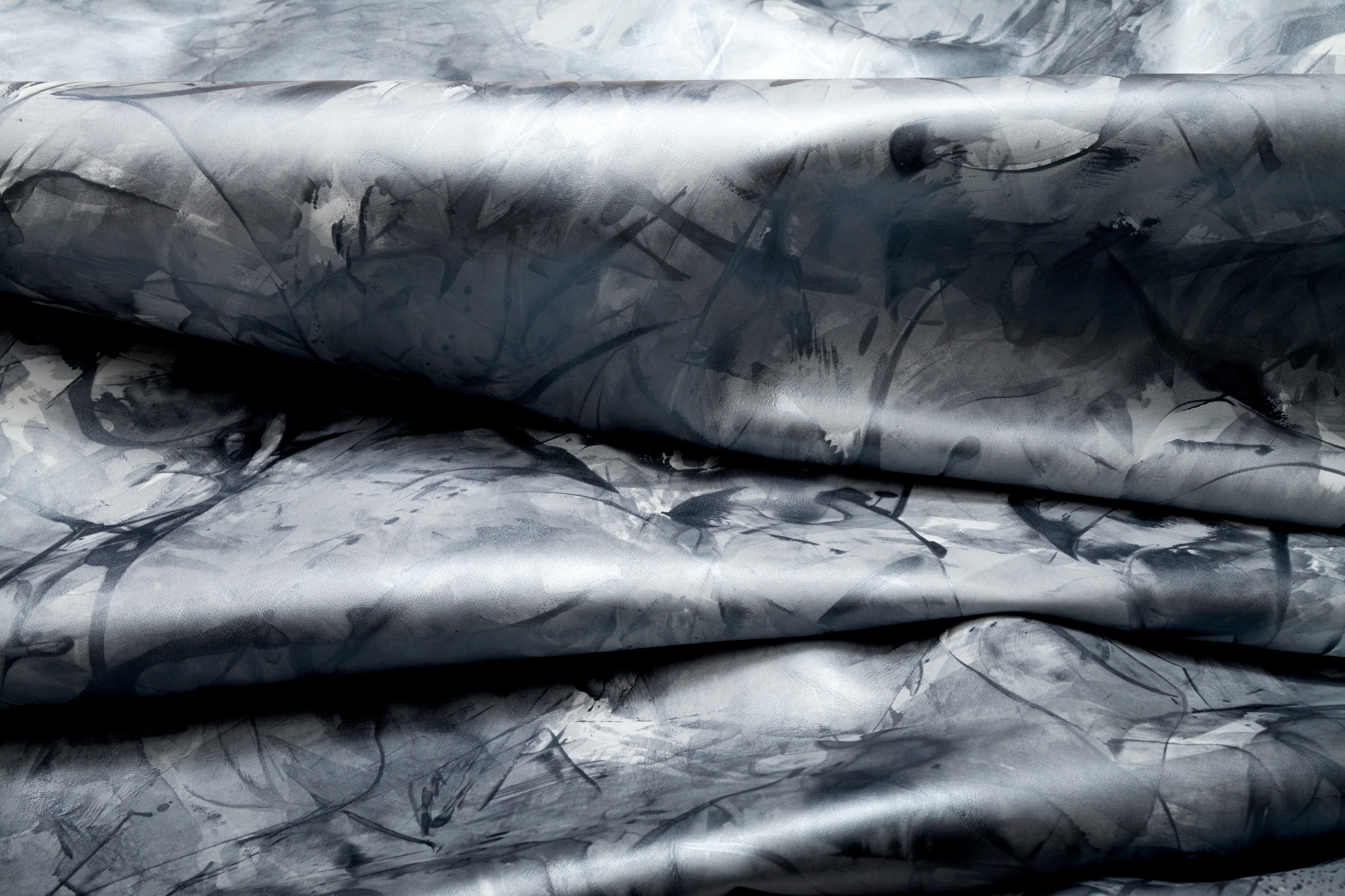 Draped upholstery leather in a mottled textural pattern in metallic gray and black.