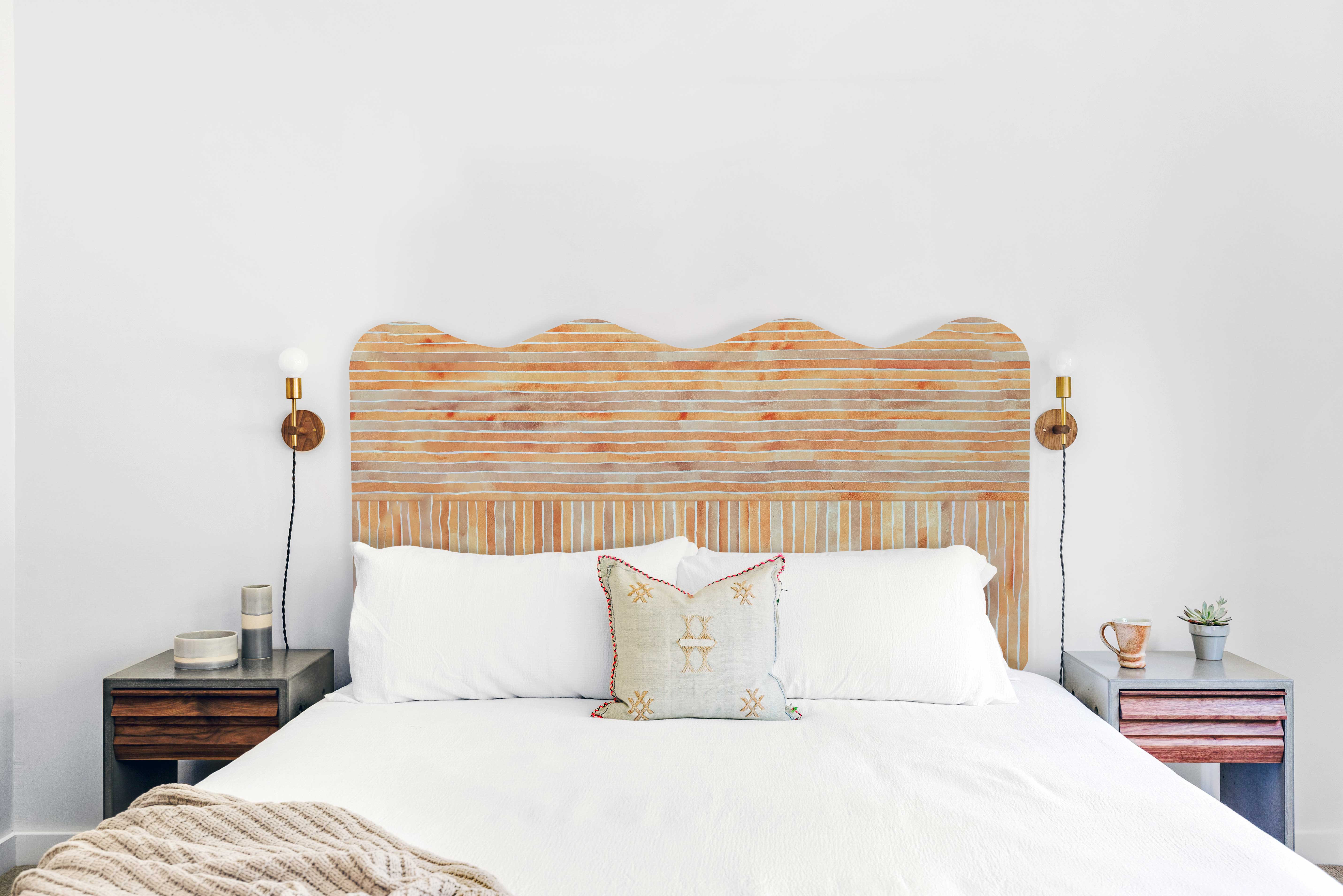 A bed with a curvilinear headboard upholstered in striped leather in mottled orange and brown.