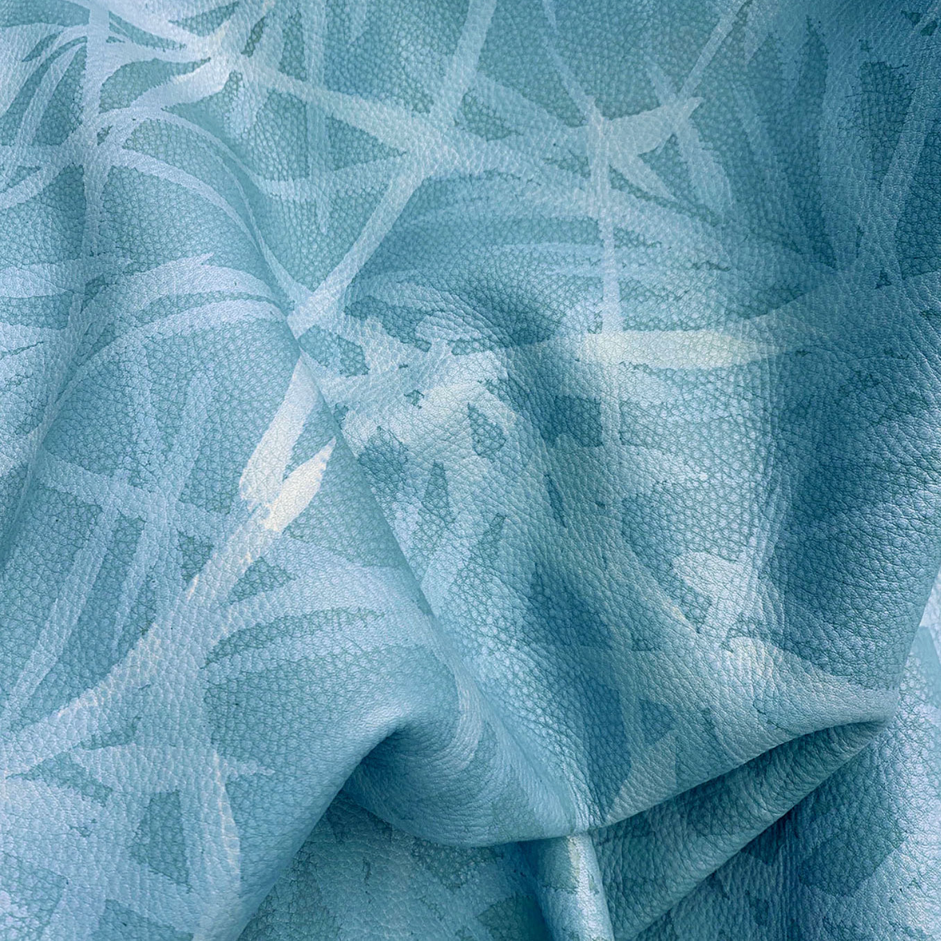 Close-up of upholstery leather in blue with a painterly botanical overlay.