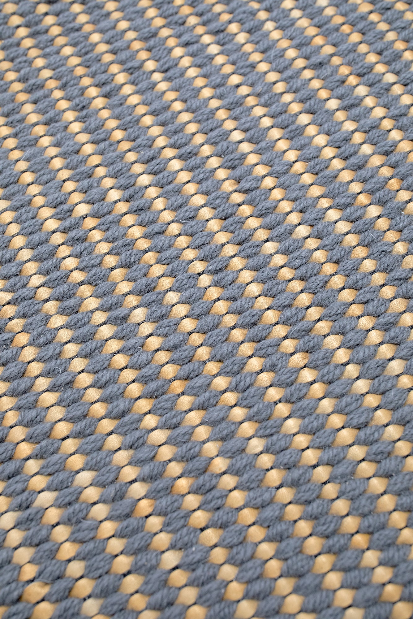 Detail of a woven leather rug in a gridded texture in gray with yellow accents.