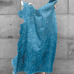 A person holding up a cowhide rug in mottled blue with a white curvilinear overlay.