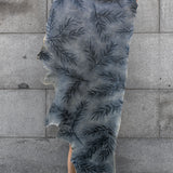 A person holding up a cowhide rug in gray with a black botanical overlay.