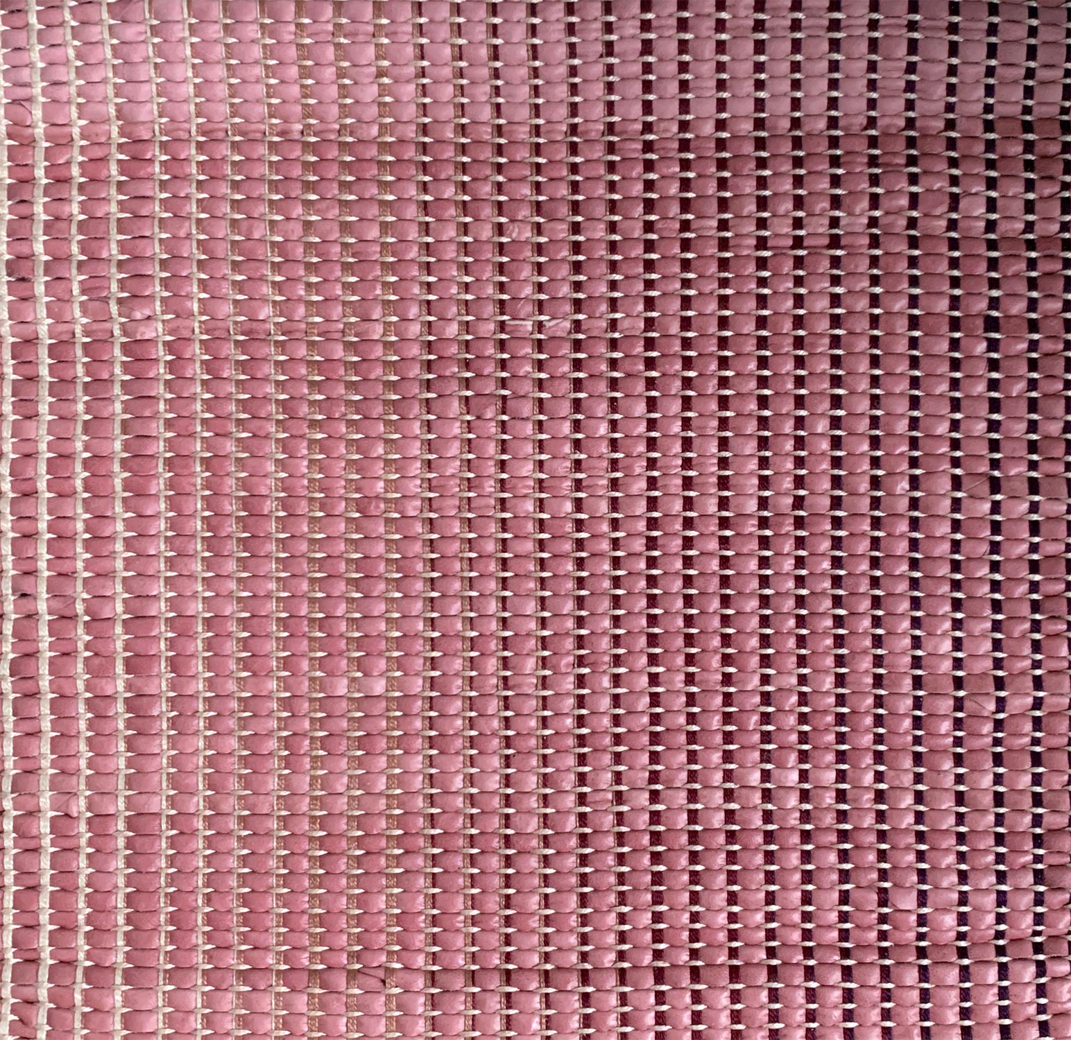 Detail of upholstery leather yardage in a grid texture in pink with black and cream accents.