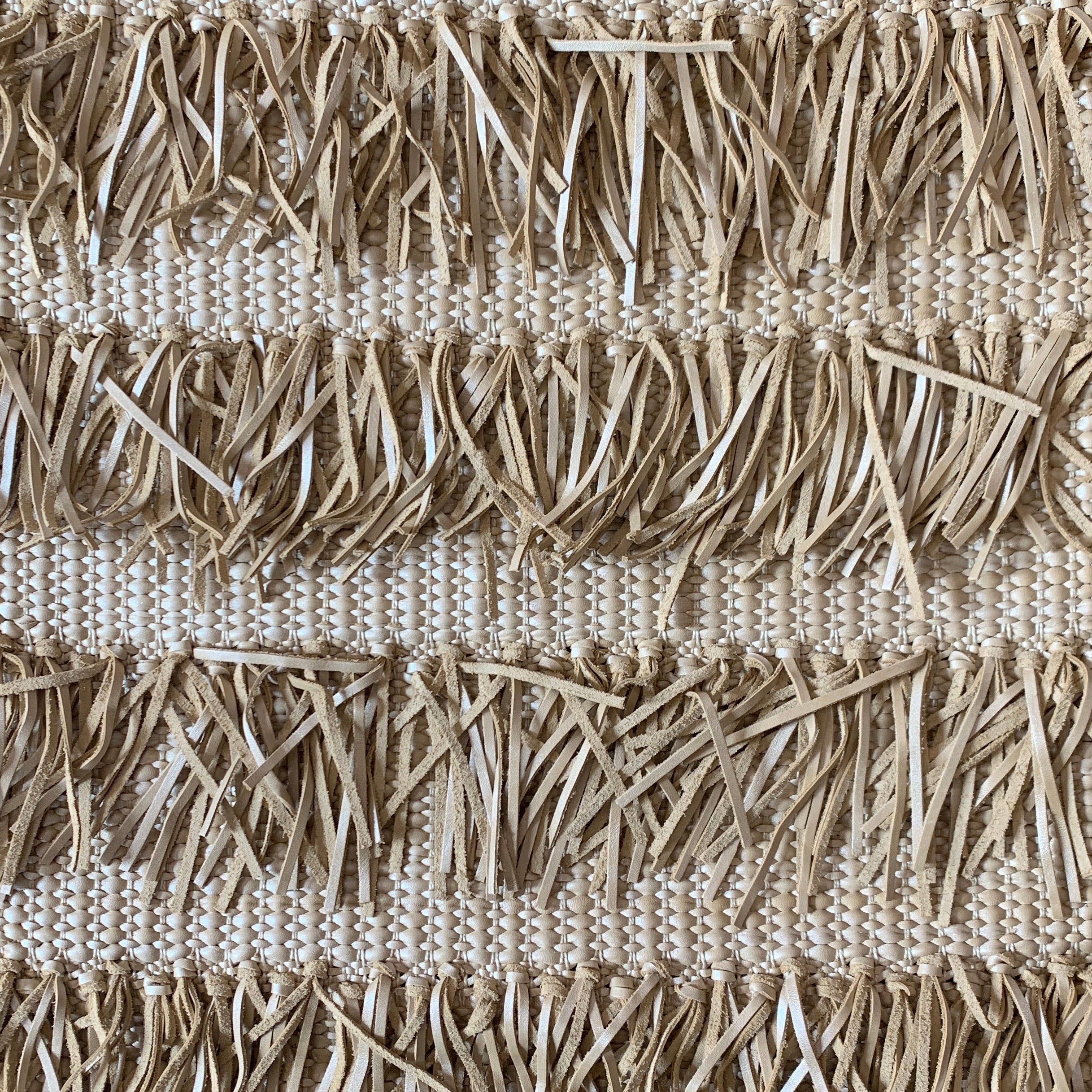 Detail of woven upholstery leather in a textured stripe and fringe pattern in cream.