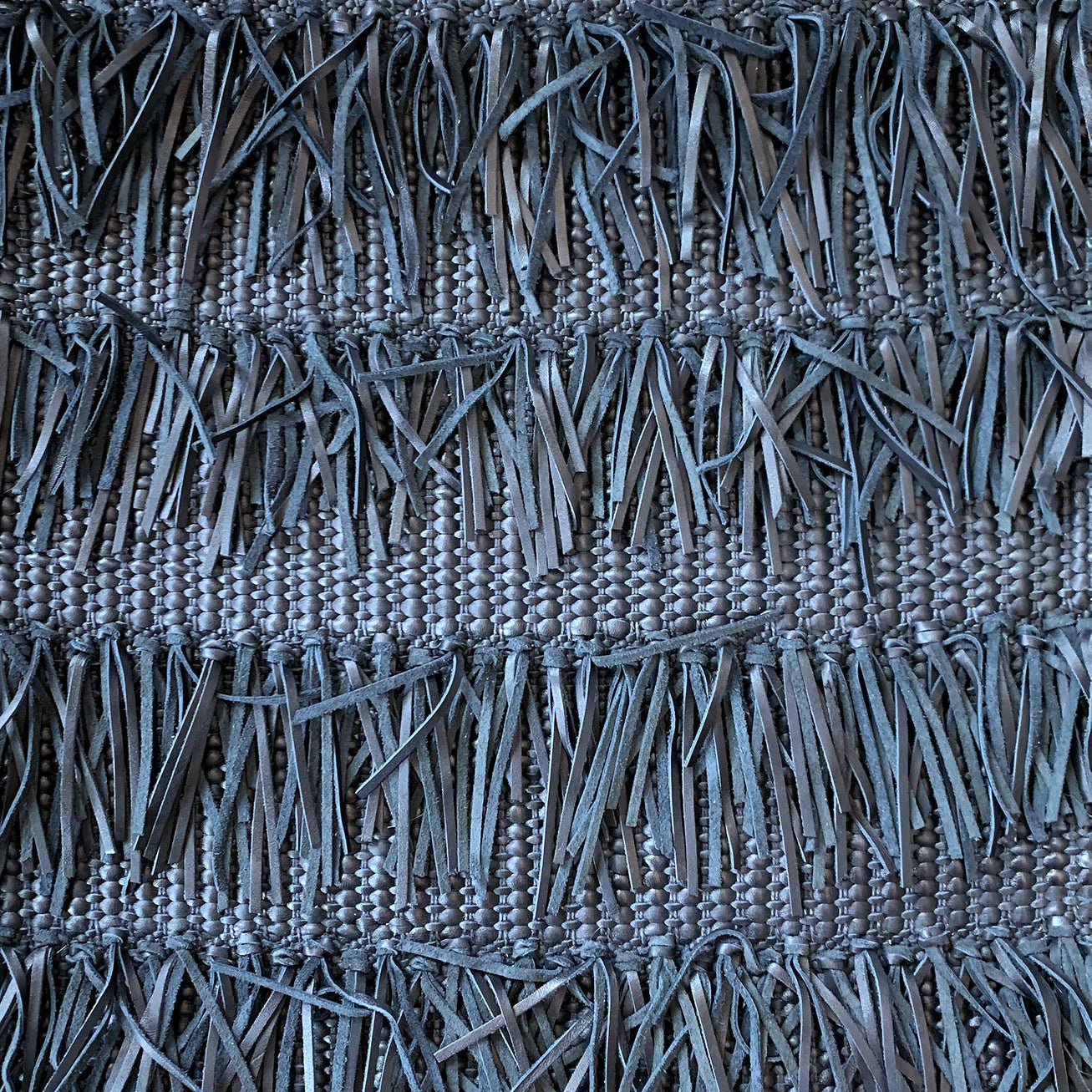 Detail of woven upholstery leather in a textured stripe and fringe pattern in navy.