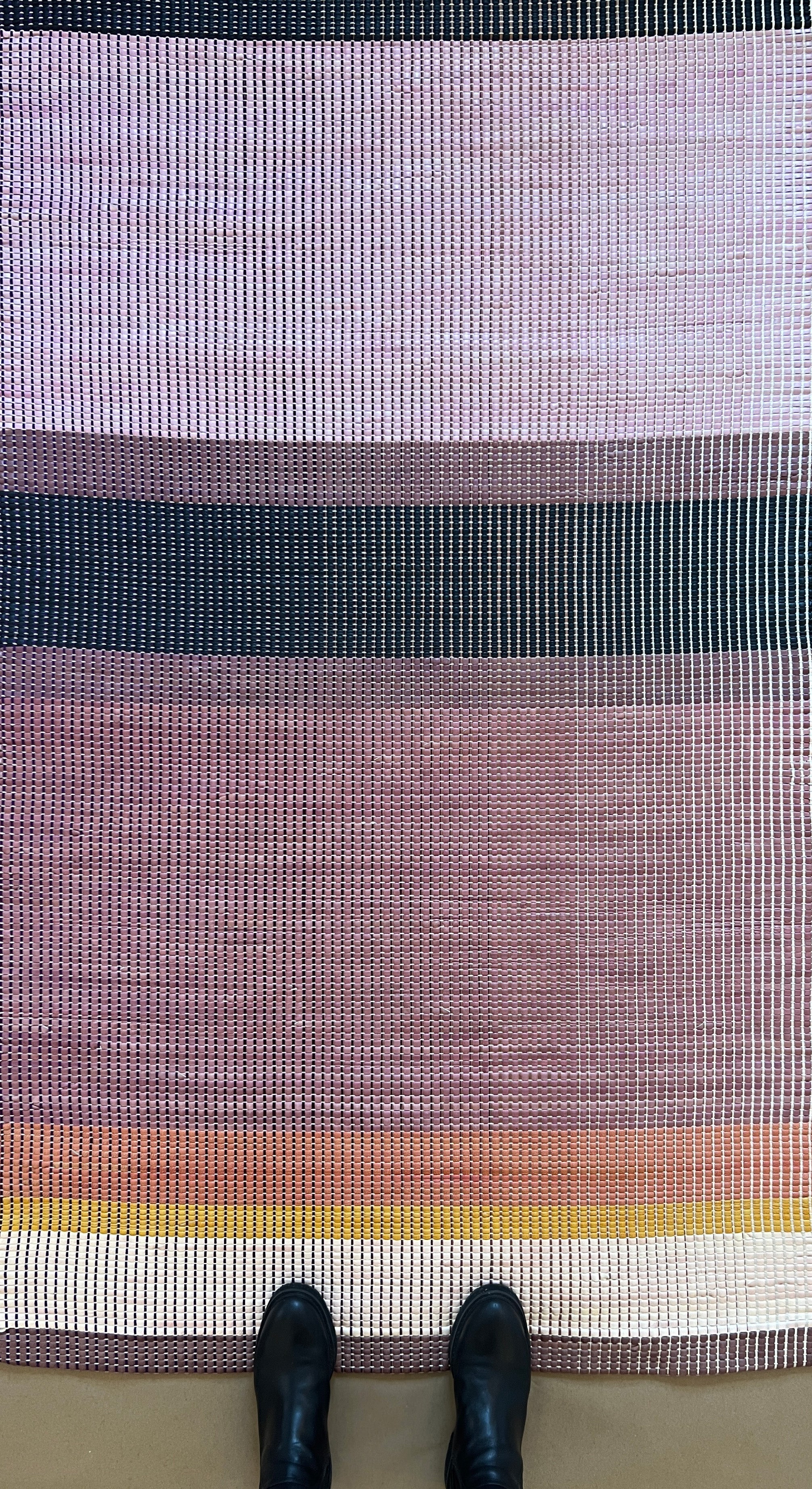 Overhead shot of a leather rug in a woven stripe pattern in shades of purple, black, coral and yellow.