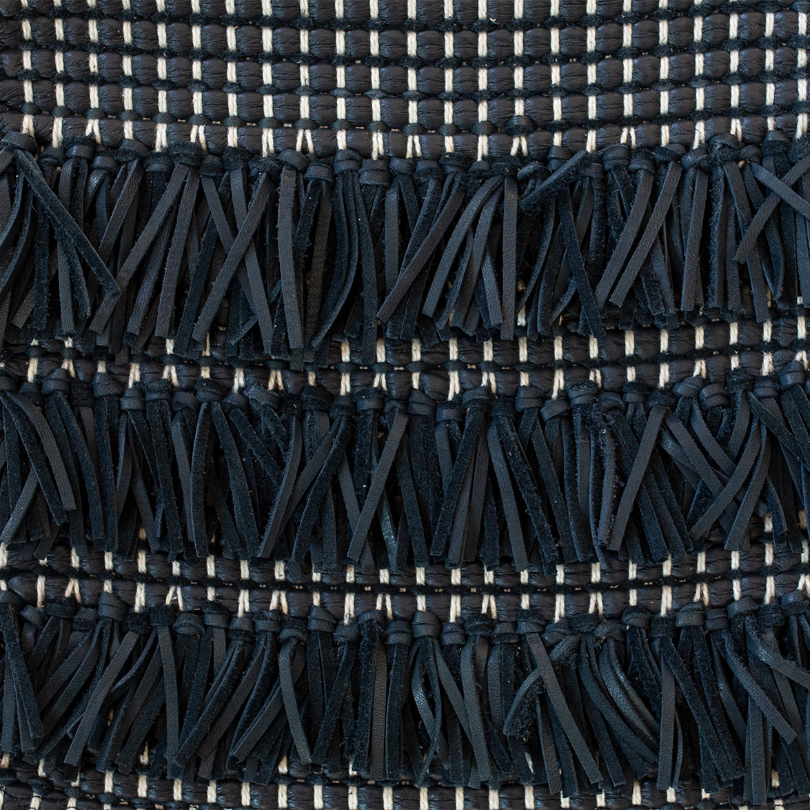 Detail of woven upholstery leather in a textured stripe and fringe pattern in navy with cream accents.