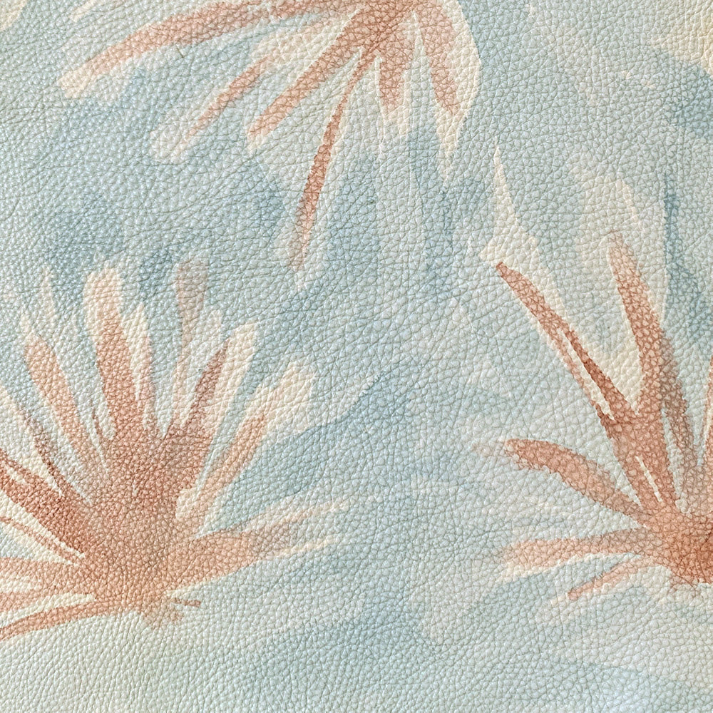 Close-up of upholstery leather in light blue with a painterly flower print in yellow and coral.