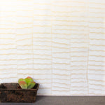 A table with a potted succulent stands in front of a wall papered in an abstract textural pattern in metallic gold and cream.