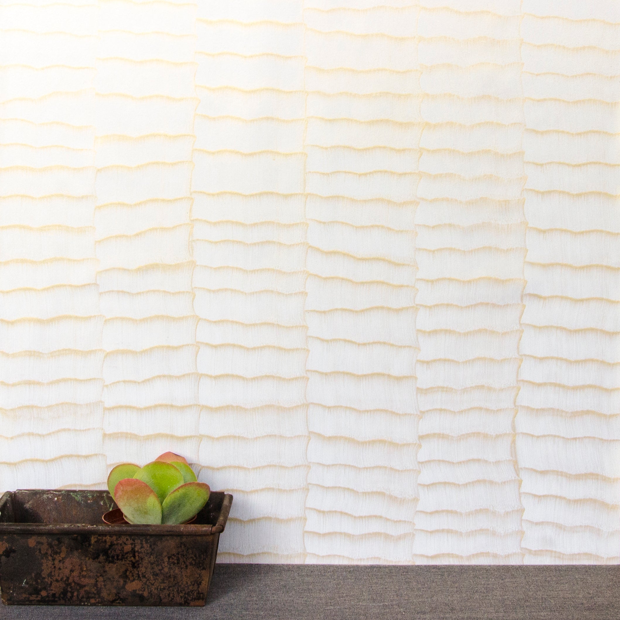 A table with a potted succulent stands in front of a wall papered in an abstract textural pattern in metallic gold and cream.