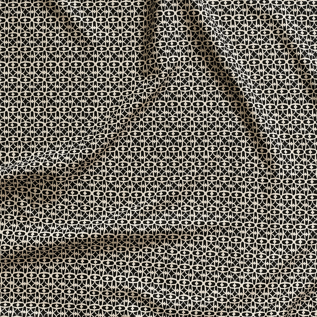Close up of gently draped fabric with small scale geometric lattice design in beige on black. 