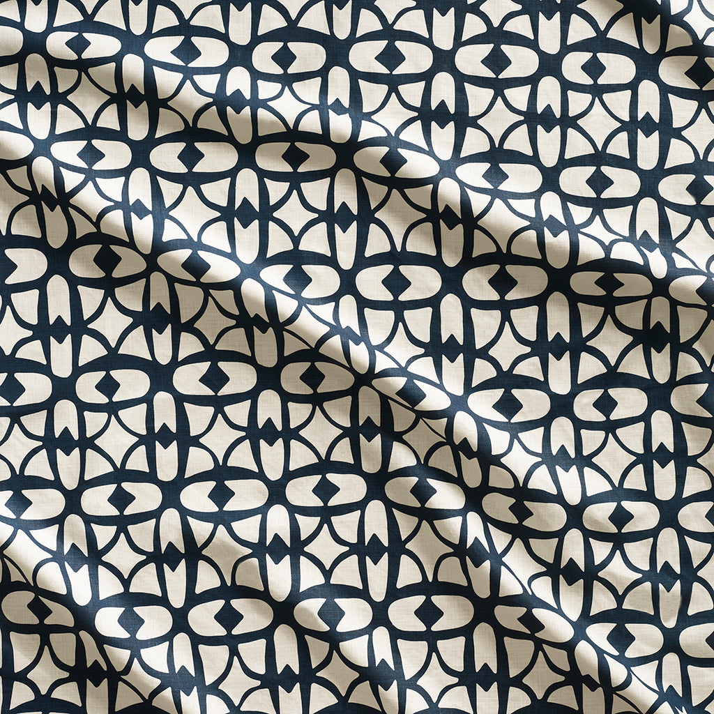 Close up of gently draped fabric with large scale geometric lattice design in cream and navy blue.
