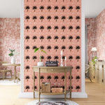A maximalist living space with an accent wall papered in a repeating palm tree print on a mottled white and coral field.