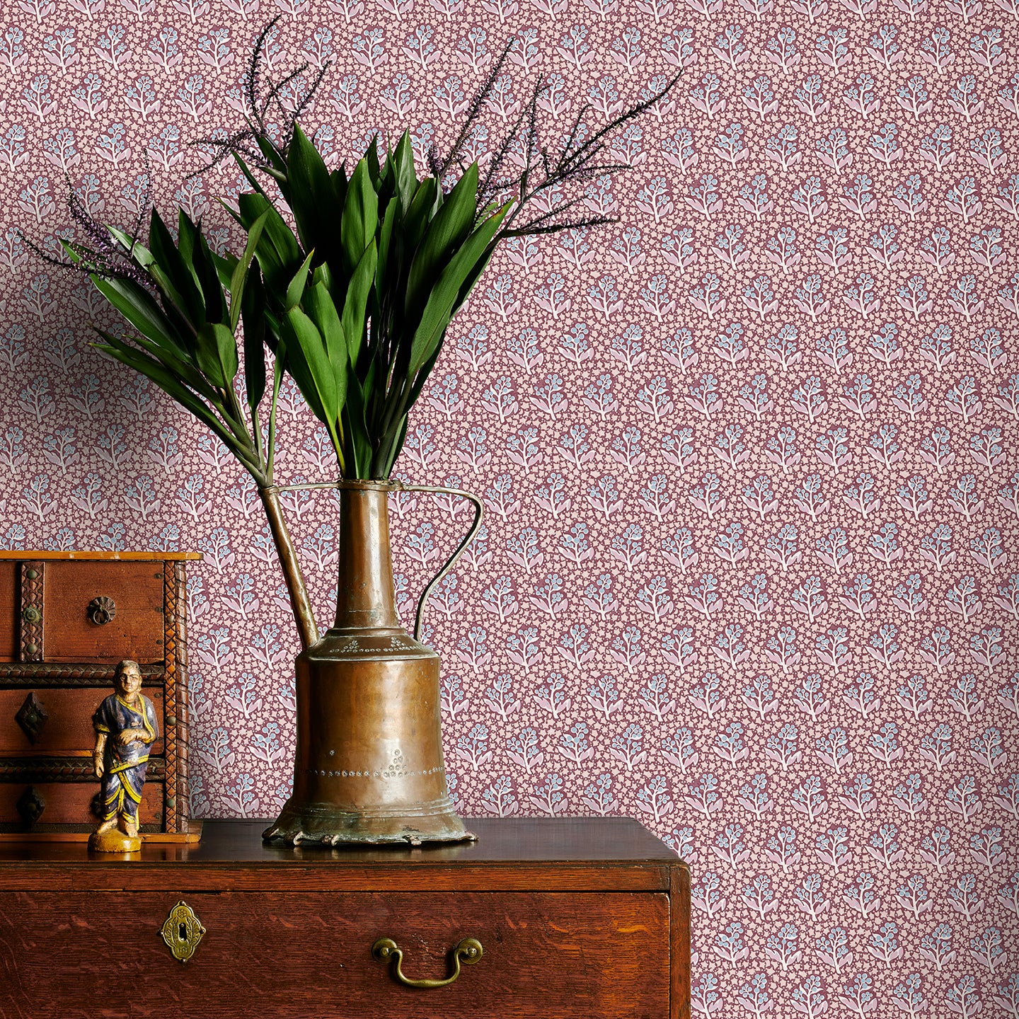 Vintage-style wallpaper with intricate patterns, a brass vase with greenery on a wooden dresser.