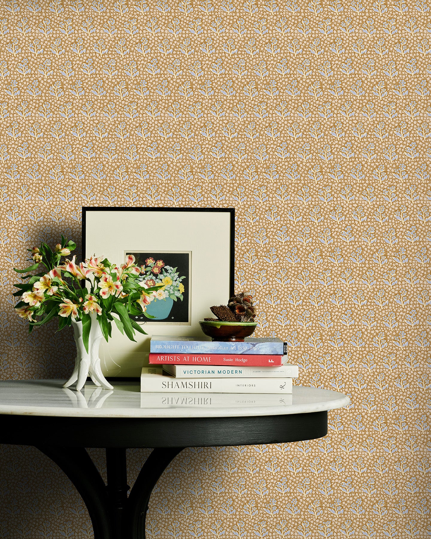 Decorative table with books and flowers against a brown and blue floral wallpaper.
