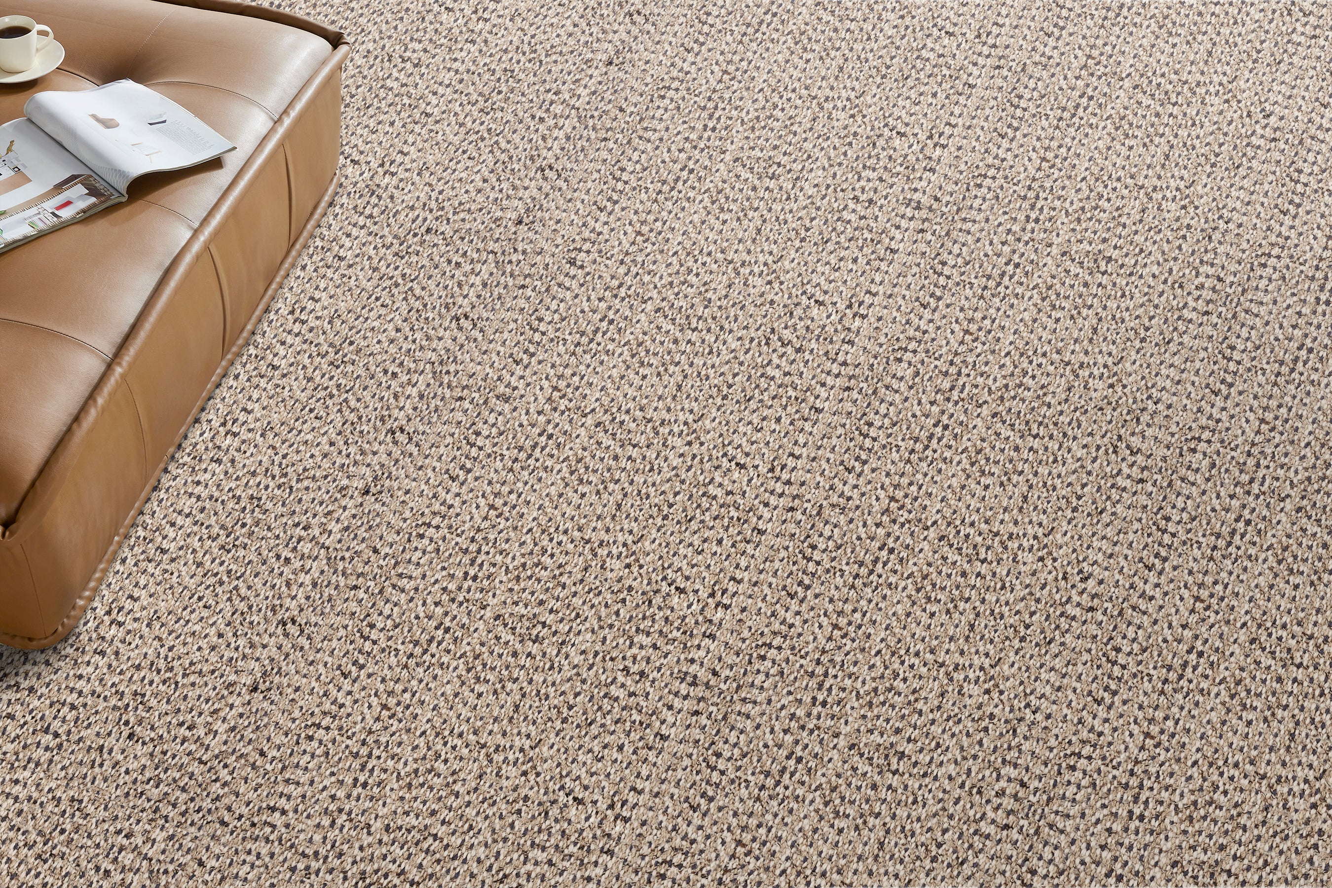 Wall to wall broadloom carpet in a textural taupe with a brown leather ottoman. 