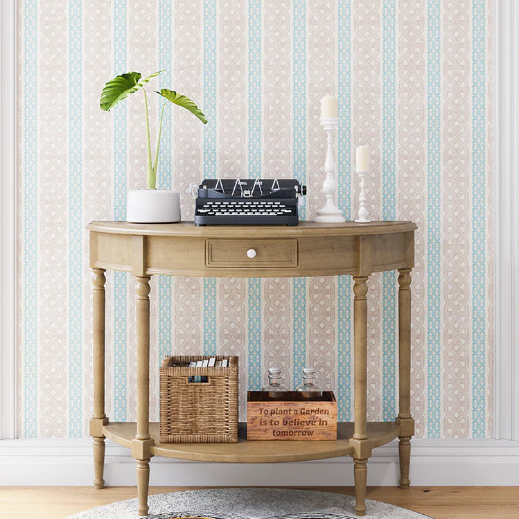 A styled end table stands in front of a wall papered in a geometric stripe print in blue, tan and cream.