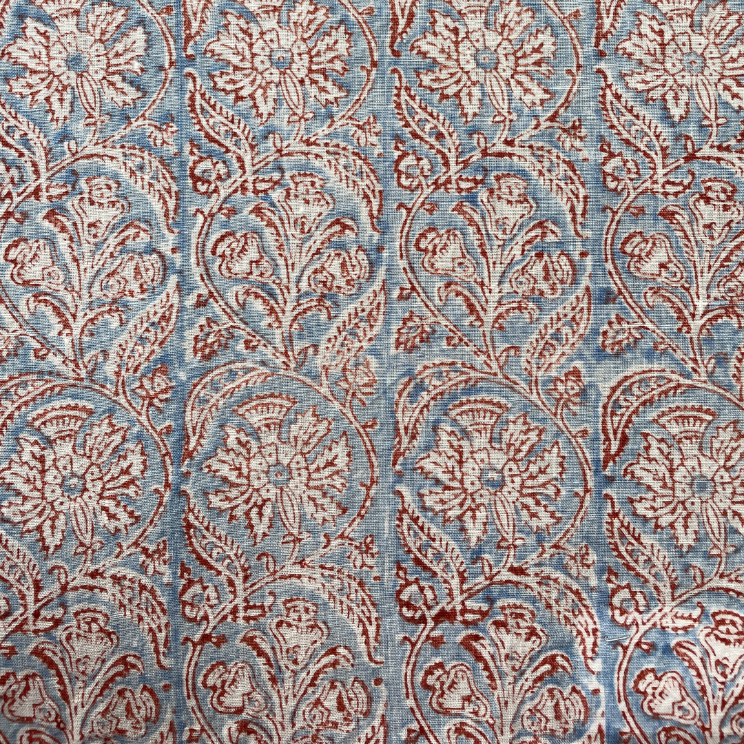 Block printed fabric in a scrolling floral stripe in red on a blue field linen
