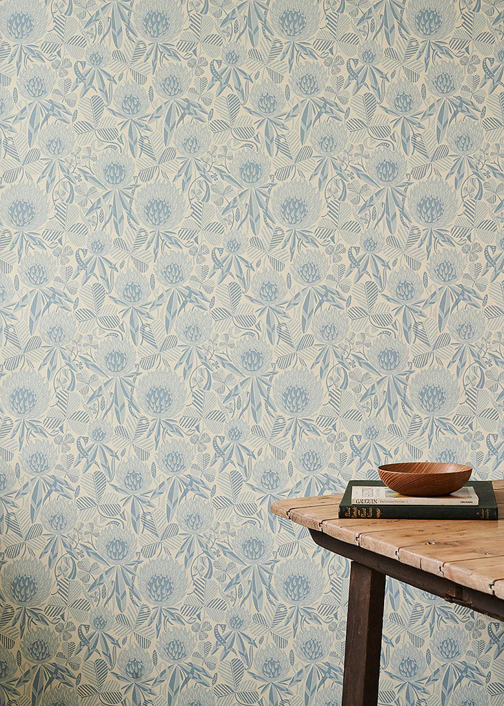Wallpaper in a a blue tonal botanical design of clover flowers and leaves, with wooden table with props.