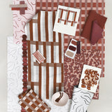 Layered mood board with printed fabrics, wallpapers, trims and swatches in shades of rust red, clay pink and cream.