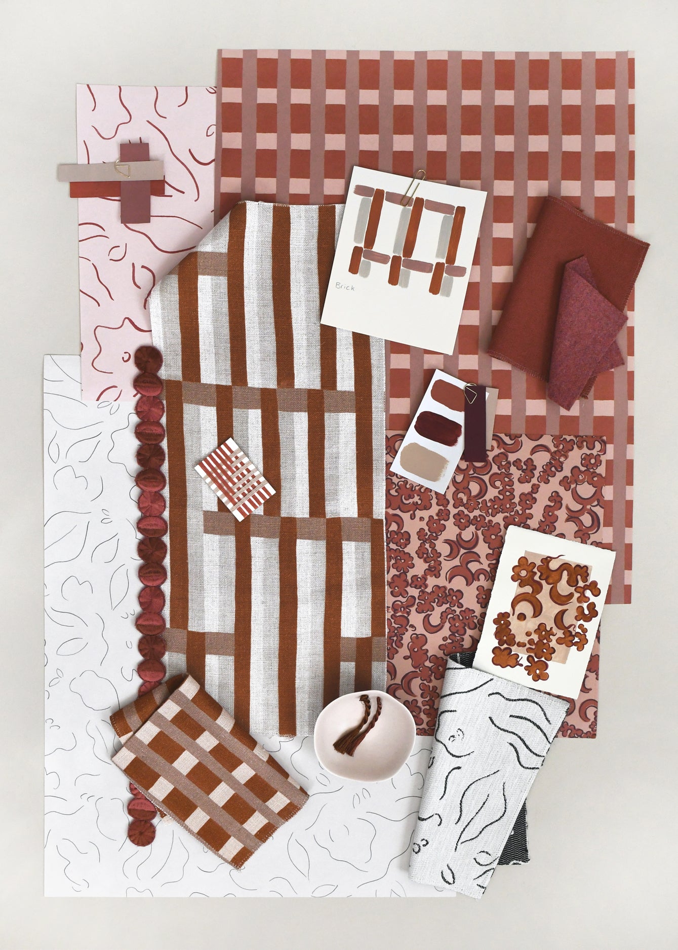 Layered mood board with printed fabrics, wallpapers, trims and swatches in shades of rust red, clay pink and cream.