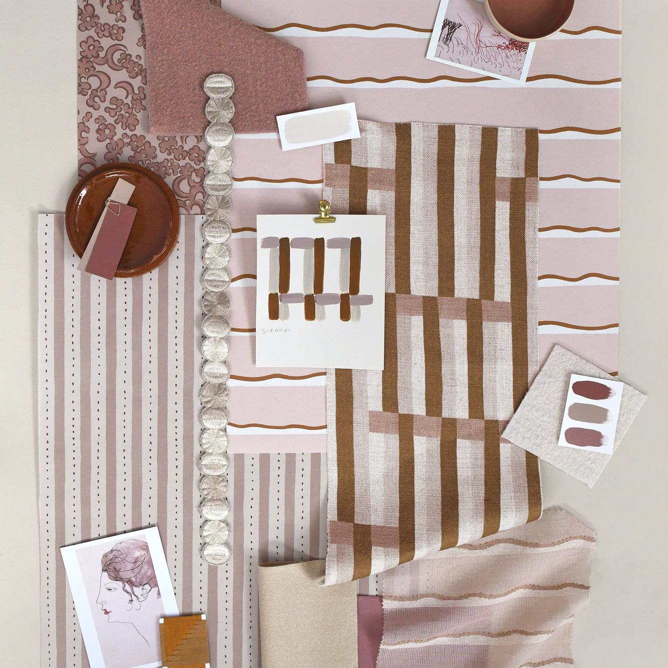 Layered mood board with printed fabrics, wallpapers, trims and swatches in shades of warm blush pinks with brown and cream accents.