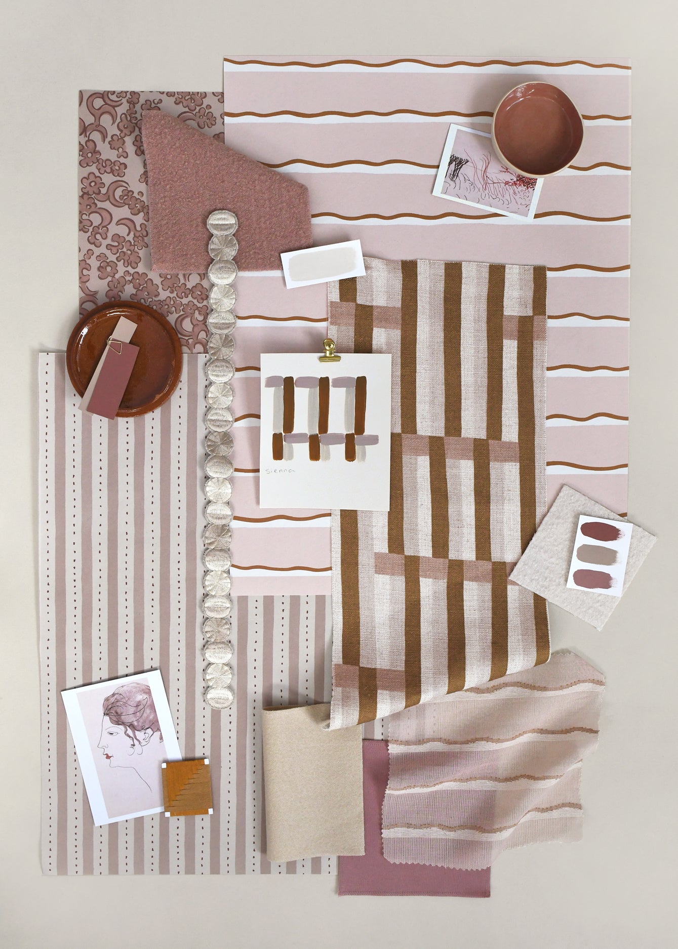 Layered mood board with printed fabrics, wallpapers, trims and swatches in shades of warm blush pinks with brown and cream accents.