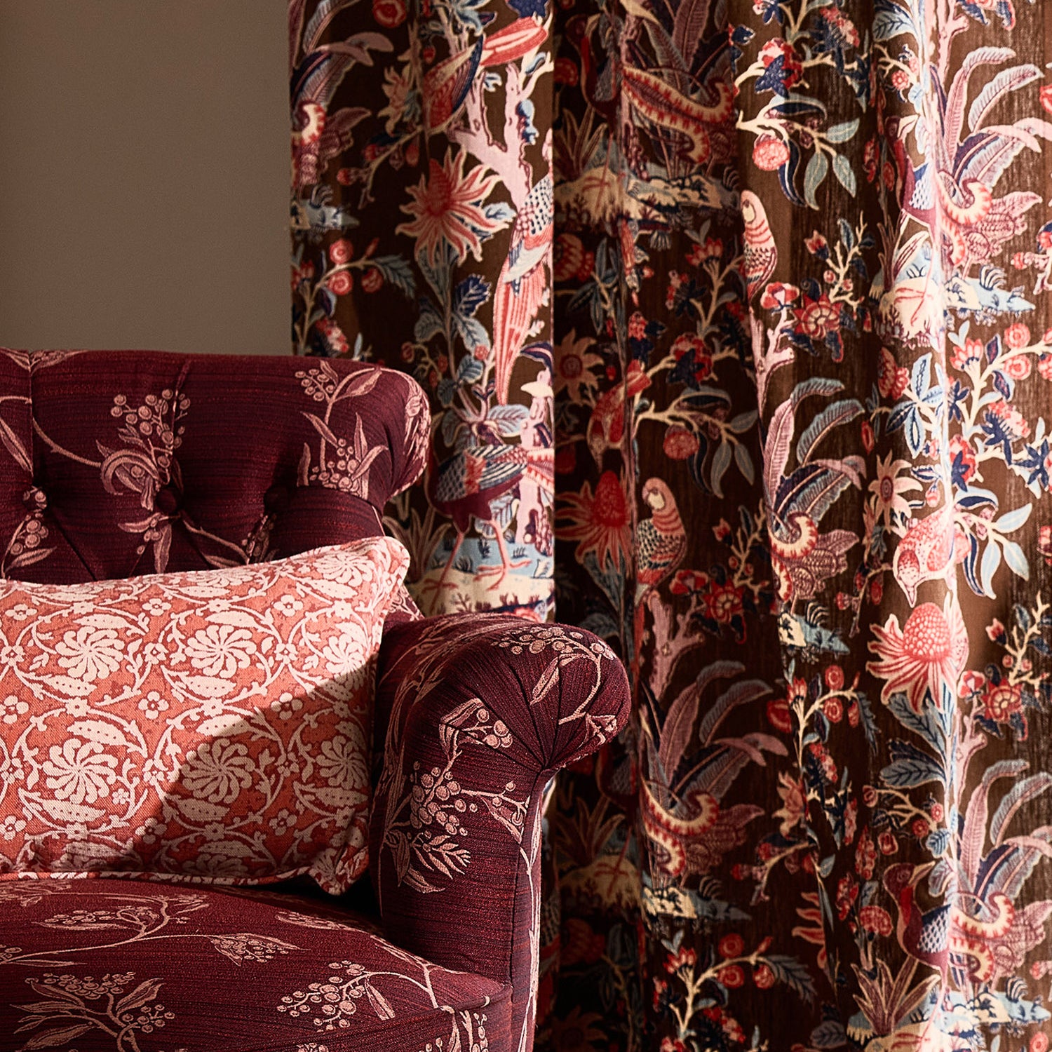Decorative armchair with floral patterned fabric against a curtain with a botanical & bird pattern.