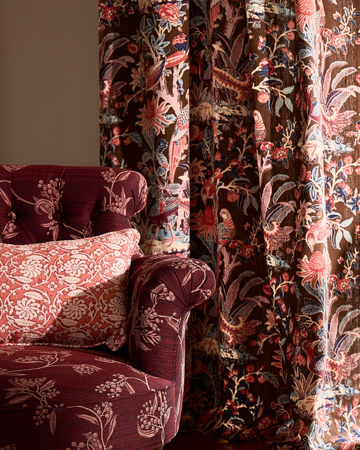 Decorative armchair with floral patterned fabric against a curtain with a botanical & bird pattern.