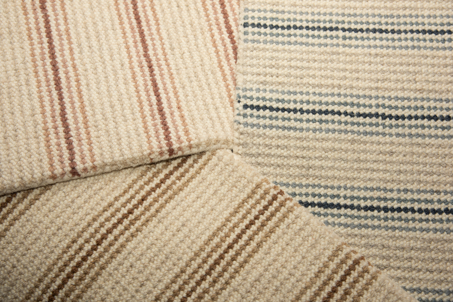 Stack of three carpet samples with widely spaced stripes in pink, blue and brown. 