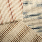 Stack of three carpet samples with widely spaced stripes in pink, blue and brown. 