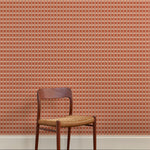 A wallpapered wall in a gridded check pattern in warm pink hues with wooden dining chair. 