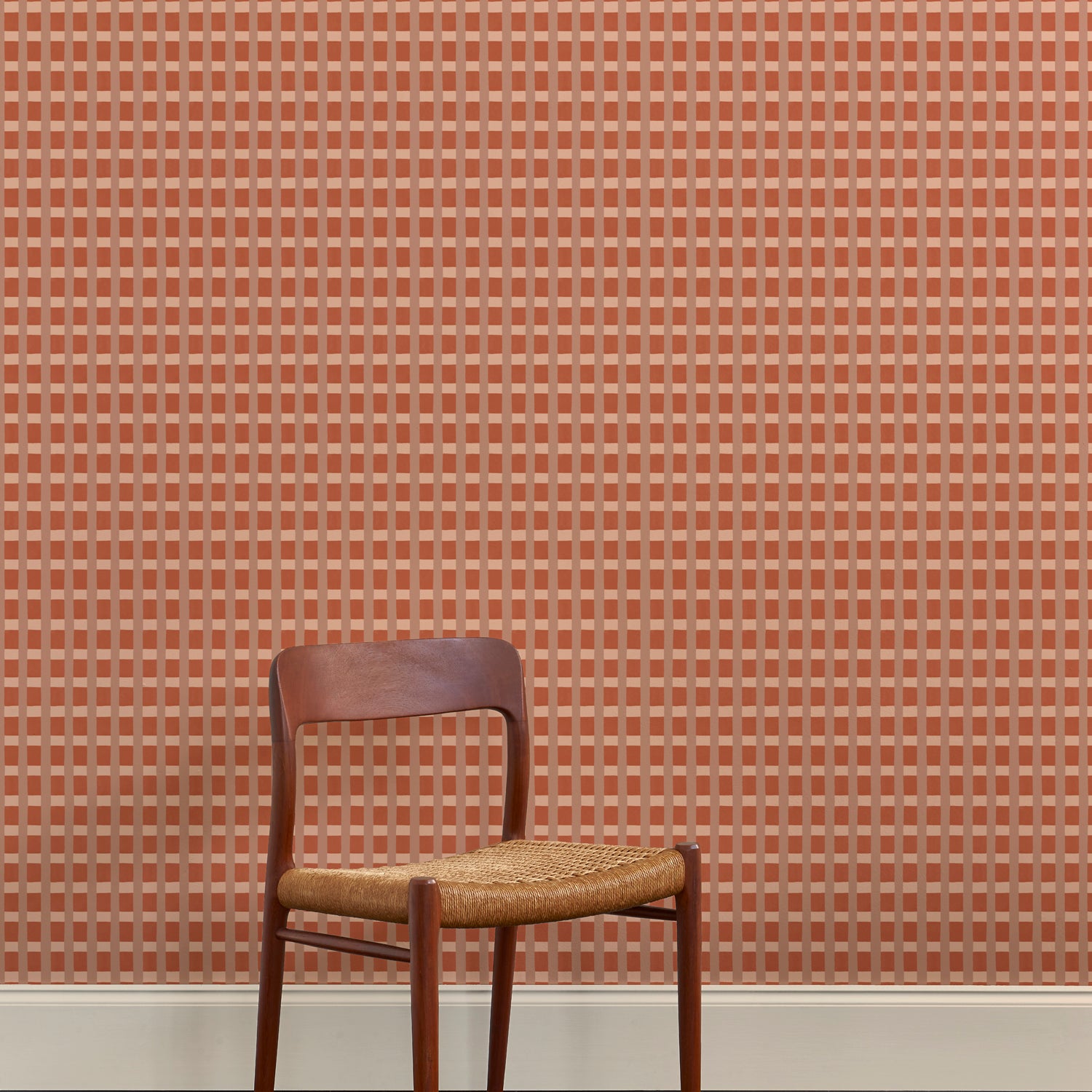 A wallpapered wall in a gridded check pattern in warm pink hues with wooden dining chair. 