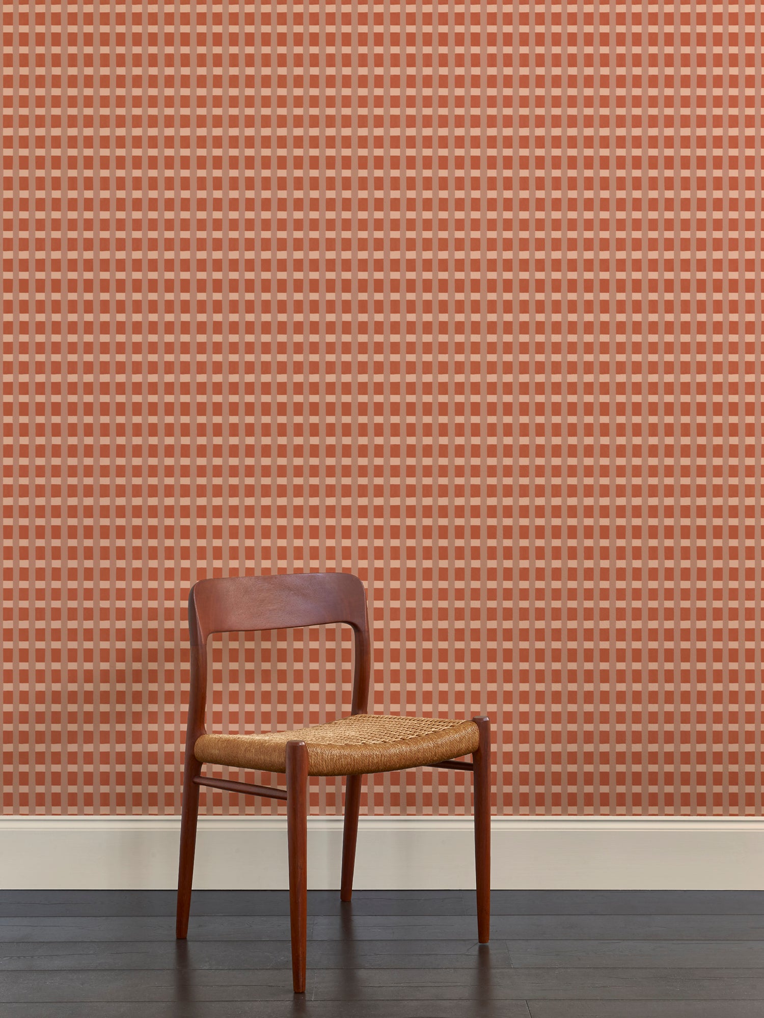 A wallpapered wall in a gridded check pattern in warm pink hues with wooden dining chair. 