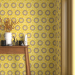 Interior with bright yellow circle printed wallpaper and matching trim with a wooden console table with white ceramic vases and mini ceramic sculptures. 