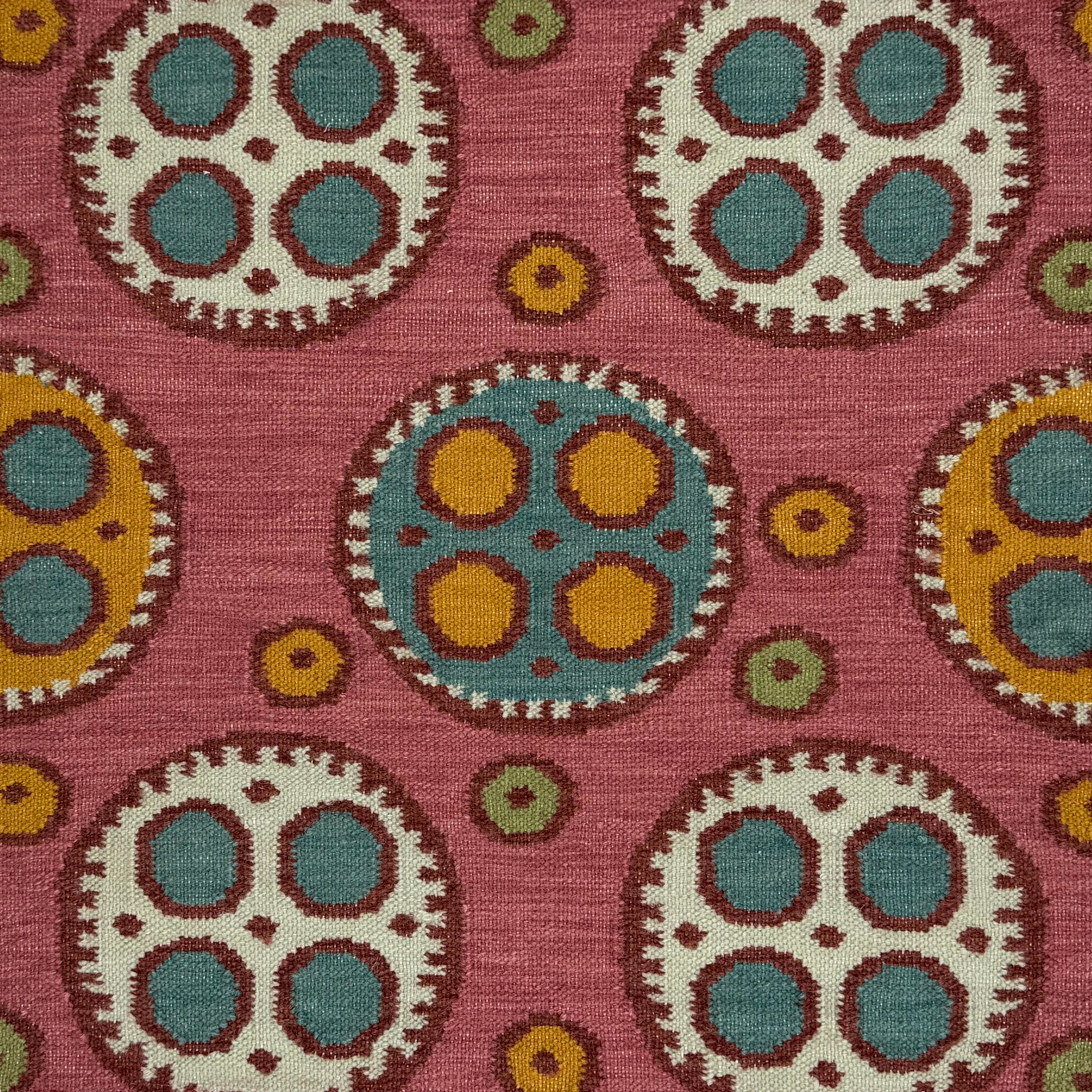 Flatweave rug with a playful polka dot pattern with a mix of sizes in cream and yellow with red outlines and smaller blue, yellow and green dots on a pink field. 