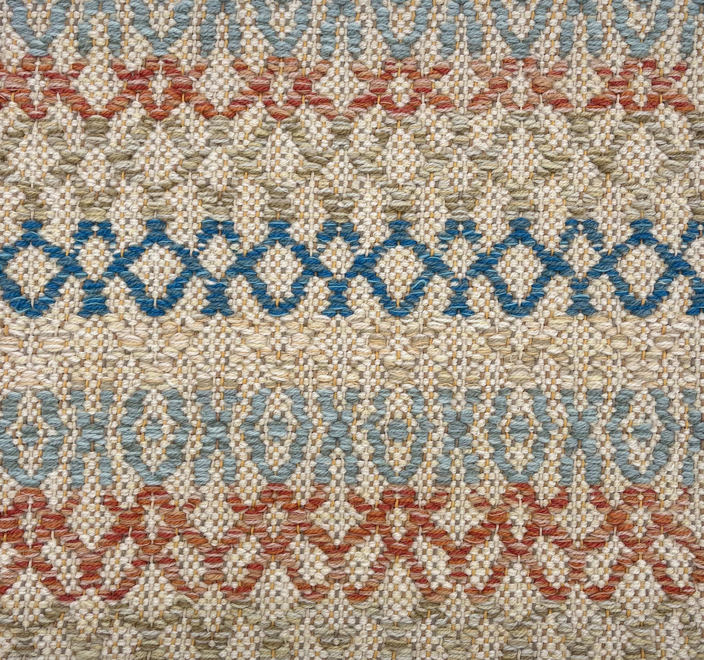 Handwoven rug detail in a lattice stripe design in blue, rust red, sage green and tan. 