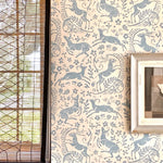 Close-up of a wall with a shuttered window and wallpaper in a deer, leaf and flower print in blue-gray and tan.