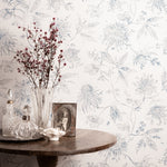 Decorative table with a vase, bottles, and photo frame against a floral wallpapered wall.