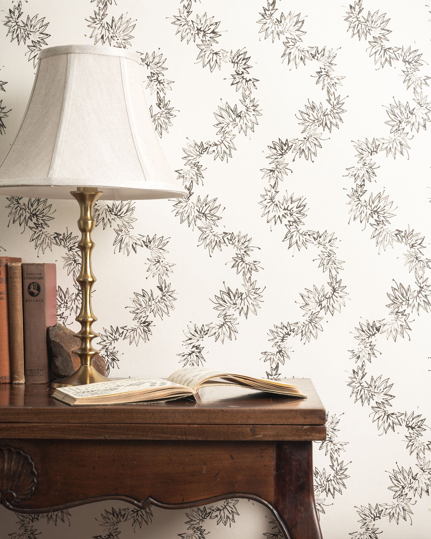 Wooden desk with lamp and books against decorative wallpaper with floral pattern.