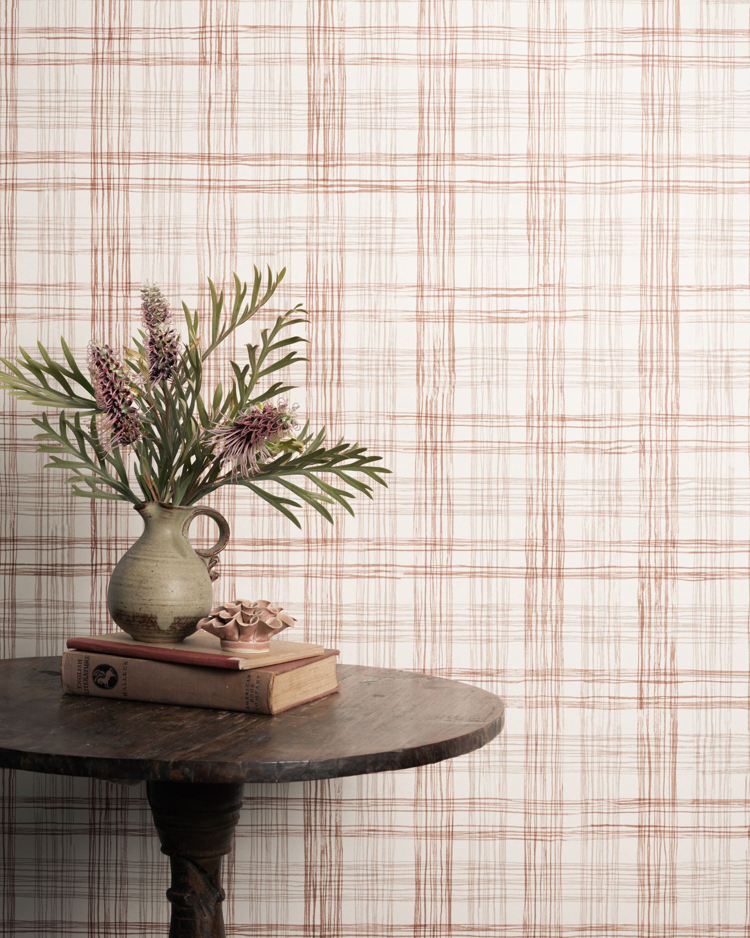 Vase with flowers and books on a table against a plaid wallpaper.