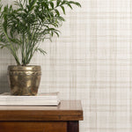 Potted plant on a wooden table against a taupe plaid wallpaper.