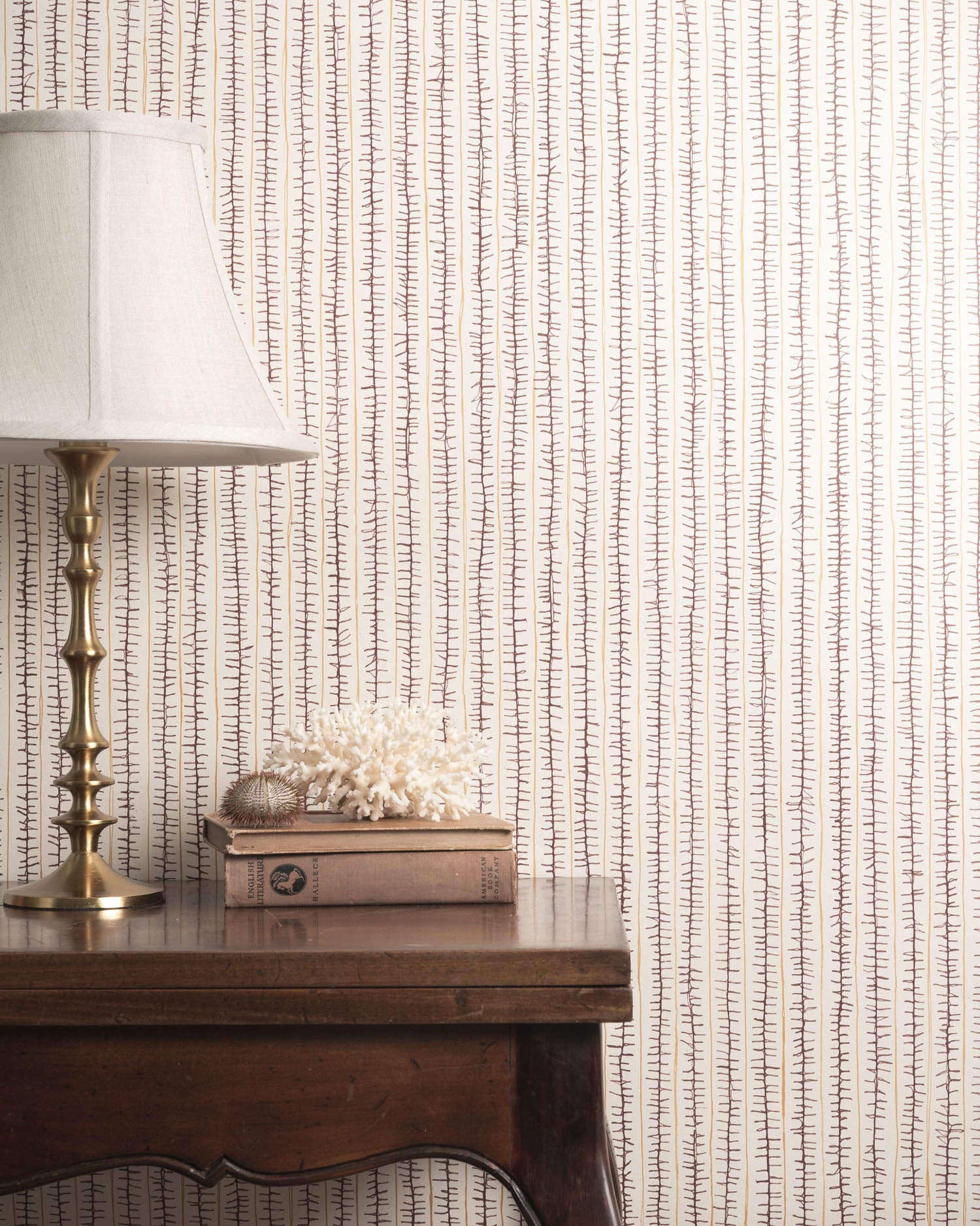 Decorative wallpaper with a subtle pattern, a lamp, and books on a wooden surface.