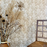 A chair and bunch of flowers stands in front of a wall papered in a dense floral print in white on a tan field.